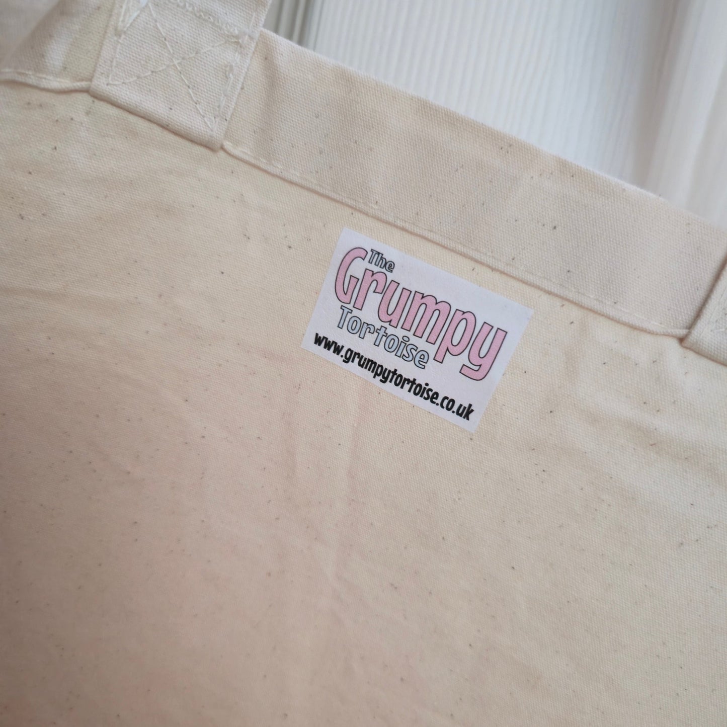 Close-up of a beige bag with a 'Grumpy' label on a white background
