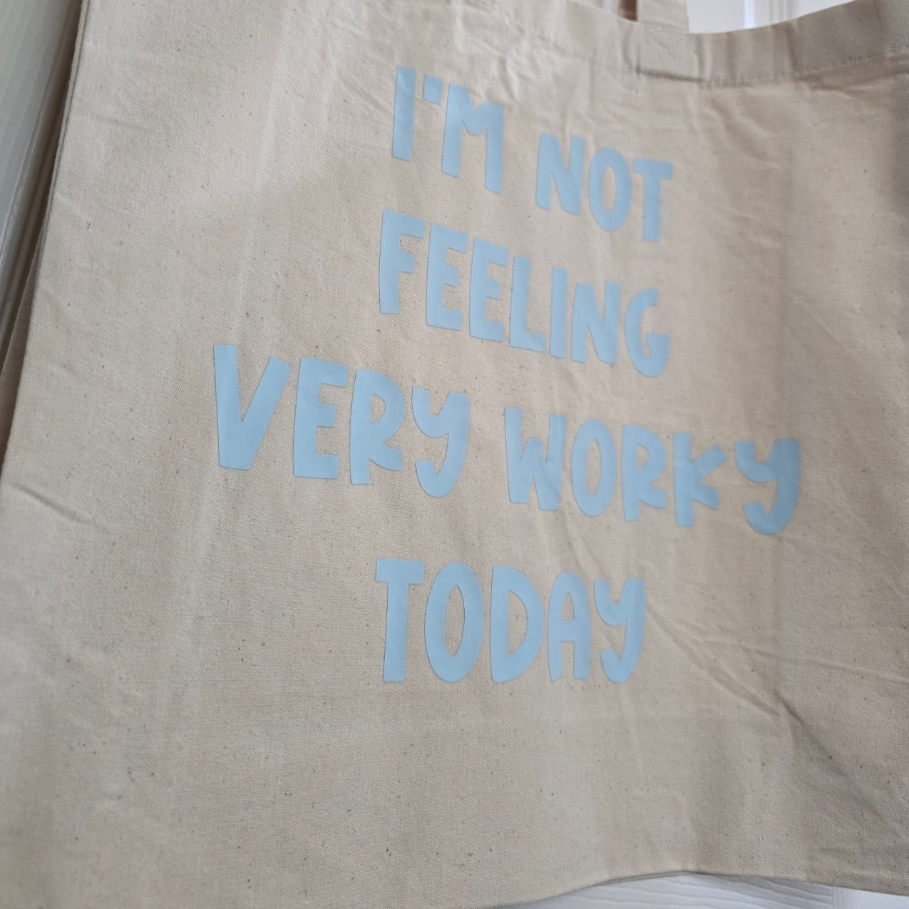 Beige tote bag with blue text 'I'm not feeling very wokey today' on a white background