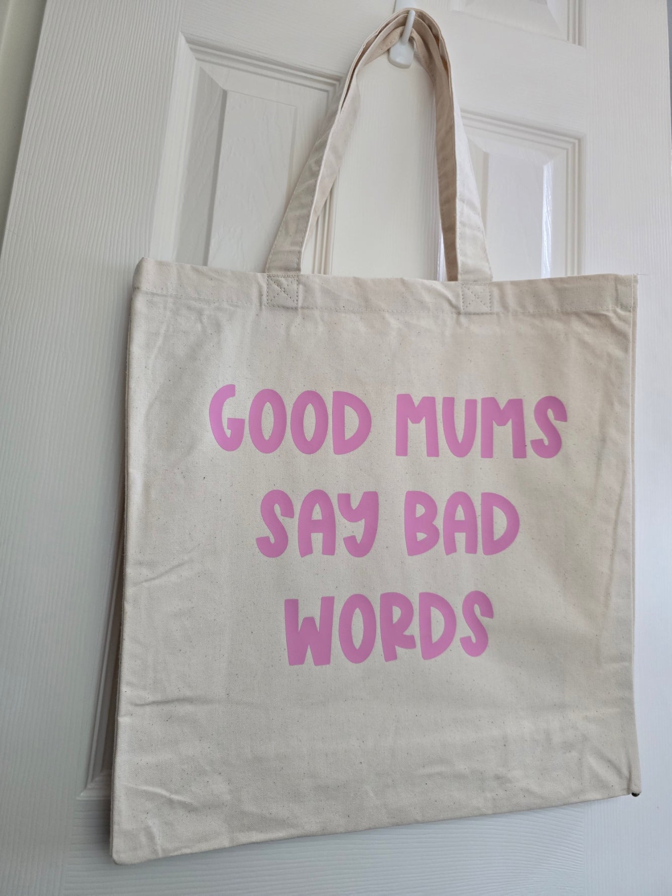 Beige tote bag with pink text 'GOOD MUMS SAY BAD WORDS' on a white background